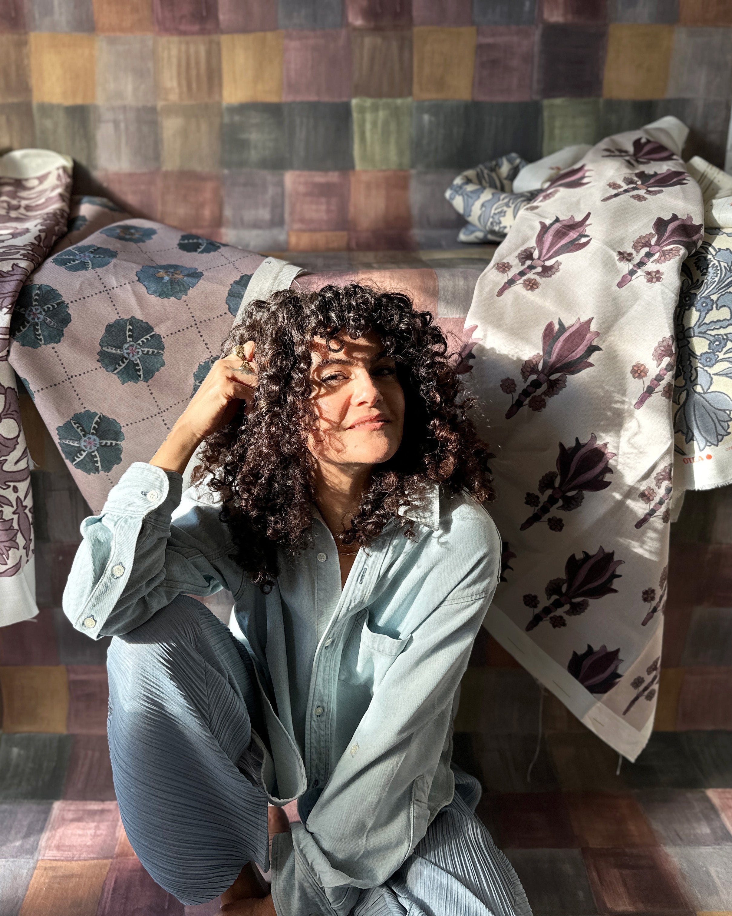 Woman sitting on a patterned wallpaper roll with a colorful patchwork wall in the background