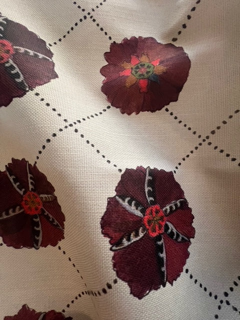 Close-up of Suzani fabric with a floral pattern in red and blue colors on a beige background.
