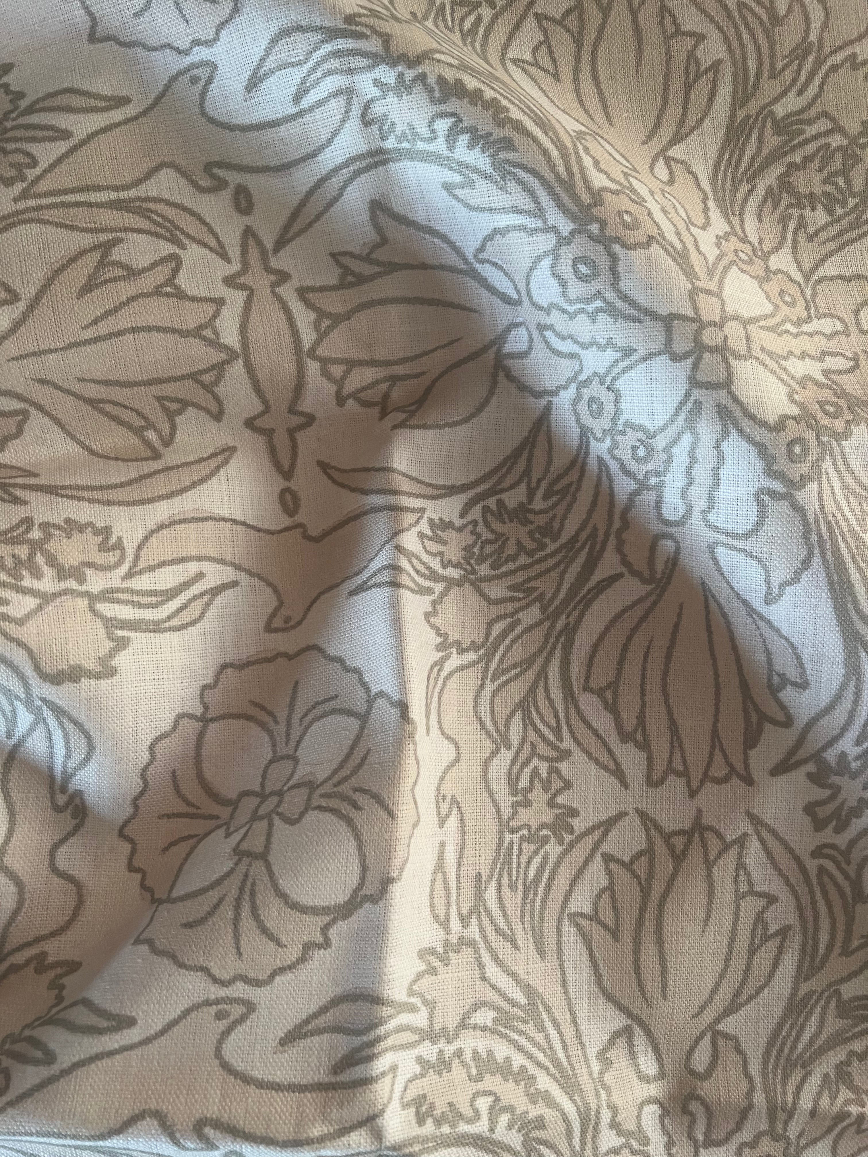 A close-up view of a vintage scarf fabric with a detailed, patterned design featuring floral and geometric elements in a soft warm white