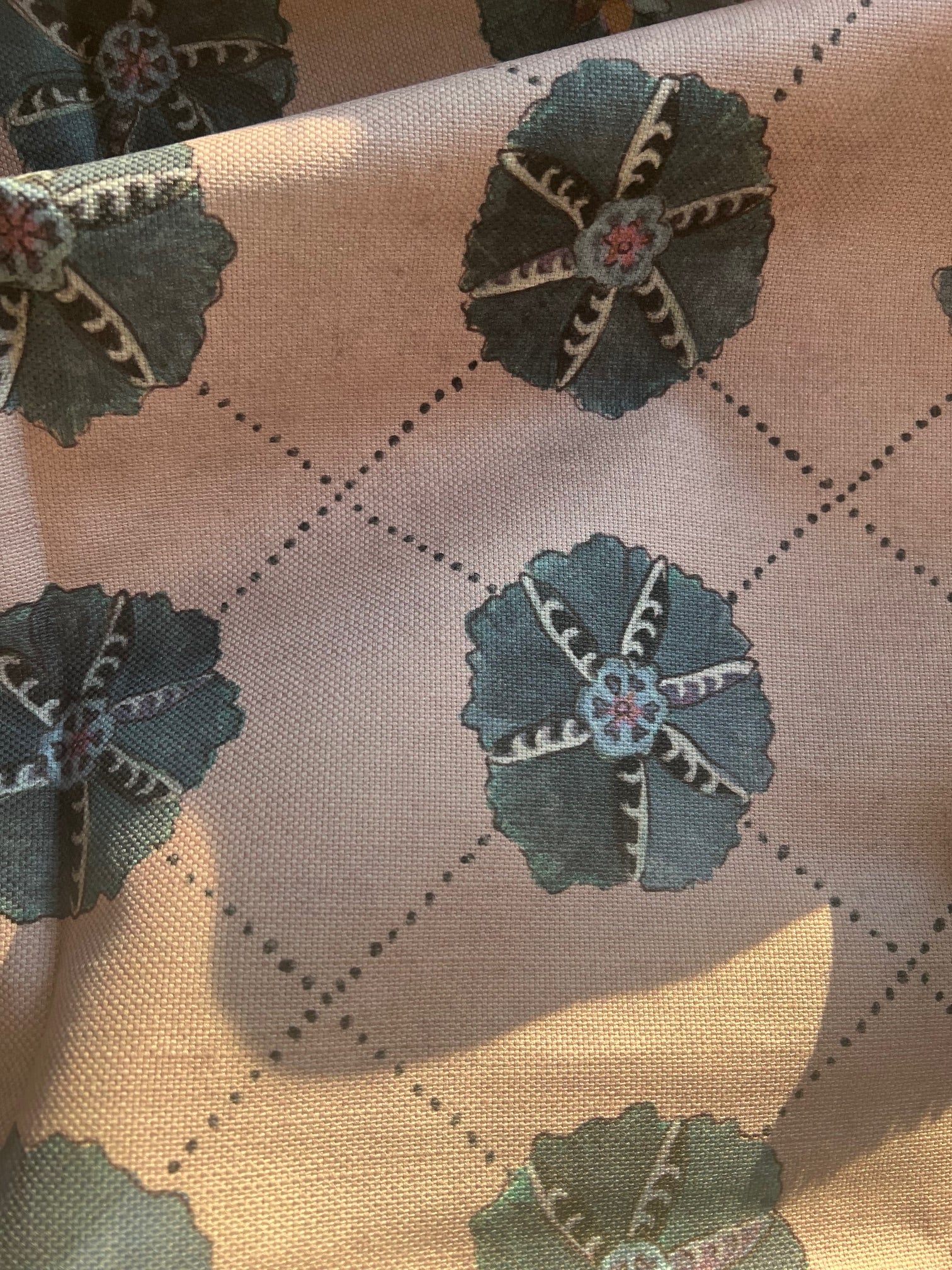 Close-up of Suzani fabric with a floral pattern in beige, blue, and green colors on a textured background.