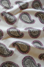 Close-up of a silk fabric with a paisley pattern featuring swirls and teardrop shapes, predominantly in beige and purple colors.