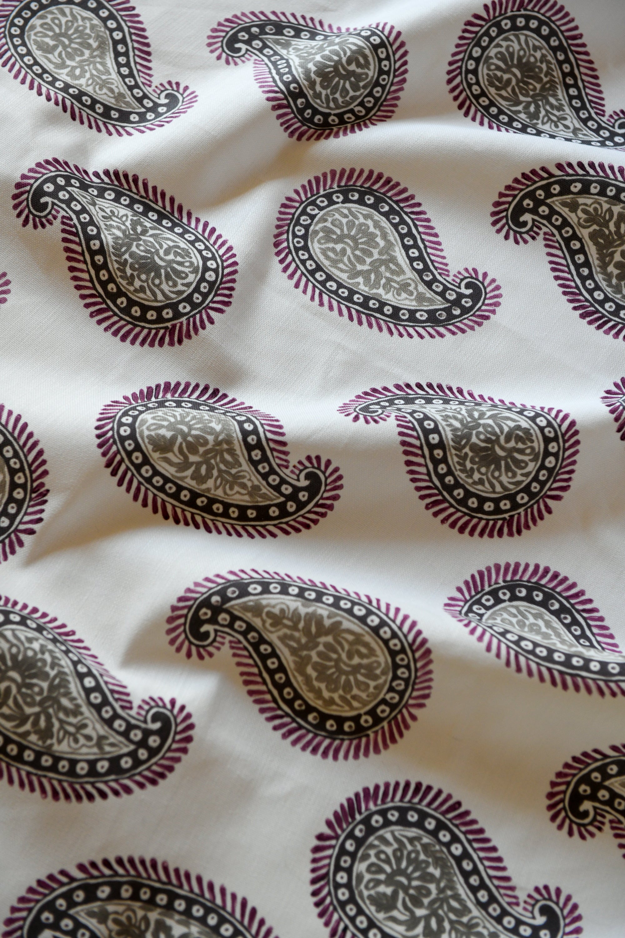 Close-up of a silk fabric with a paisley pattern featuring swirls and teardrop shapes, predominantly in beige and purple colors.