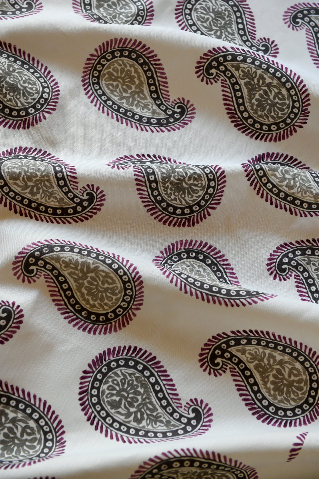 Close-up of a silk fabric with a paisley pattern featuring swirls and teardrop shapes, predominantly in beige and purple colors.