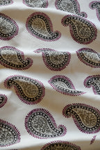 Close-up of a silk fabric with a paisley pattern featuring swirls and teardrop shapes, predominantly in beige and purple colors.