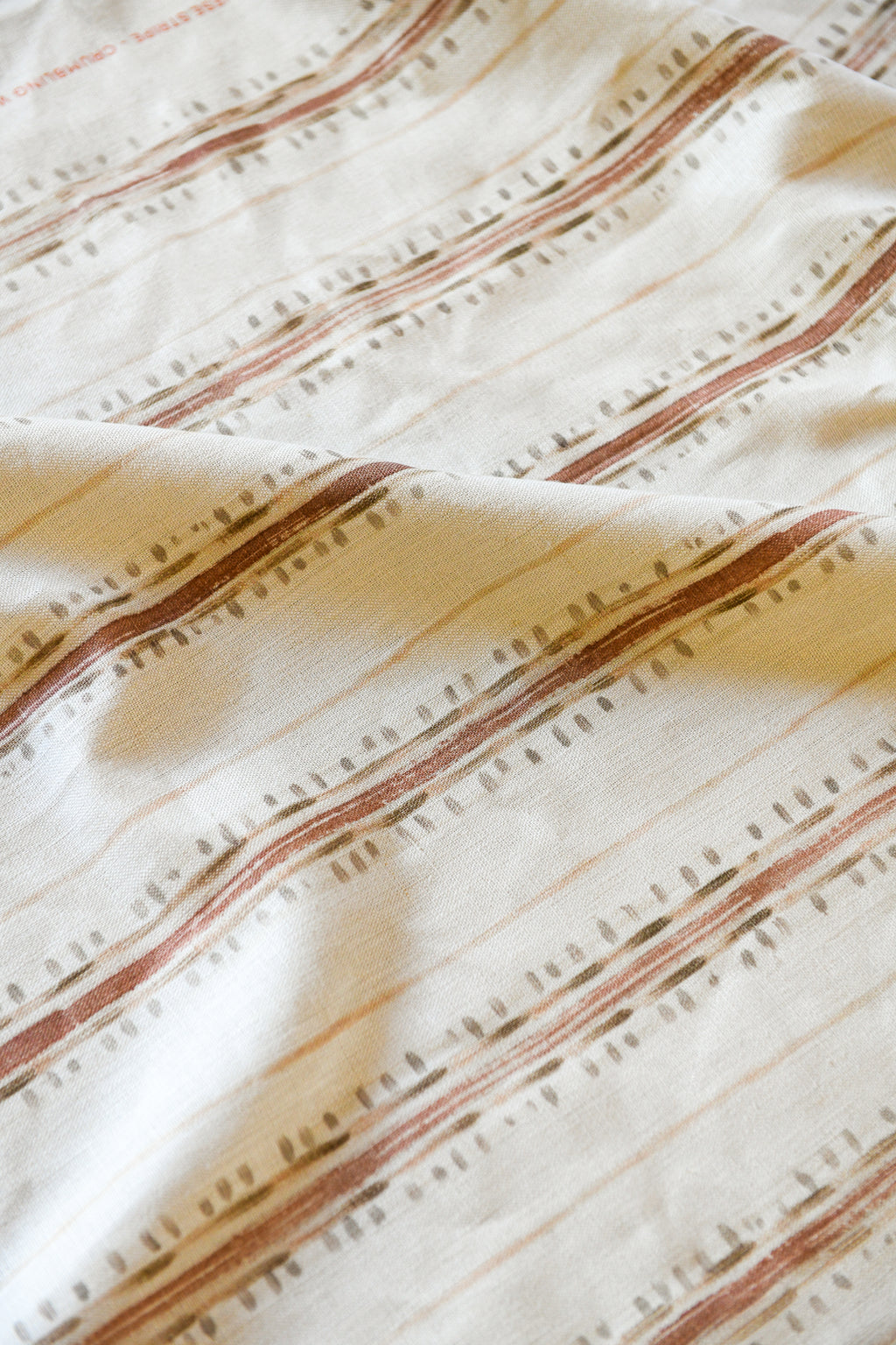 Close-up view of a striped pattern fabric with beige and brown colors, showcasing the texture and subtle details of the material.
