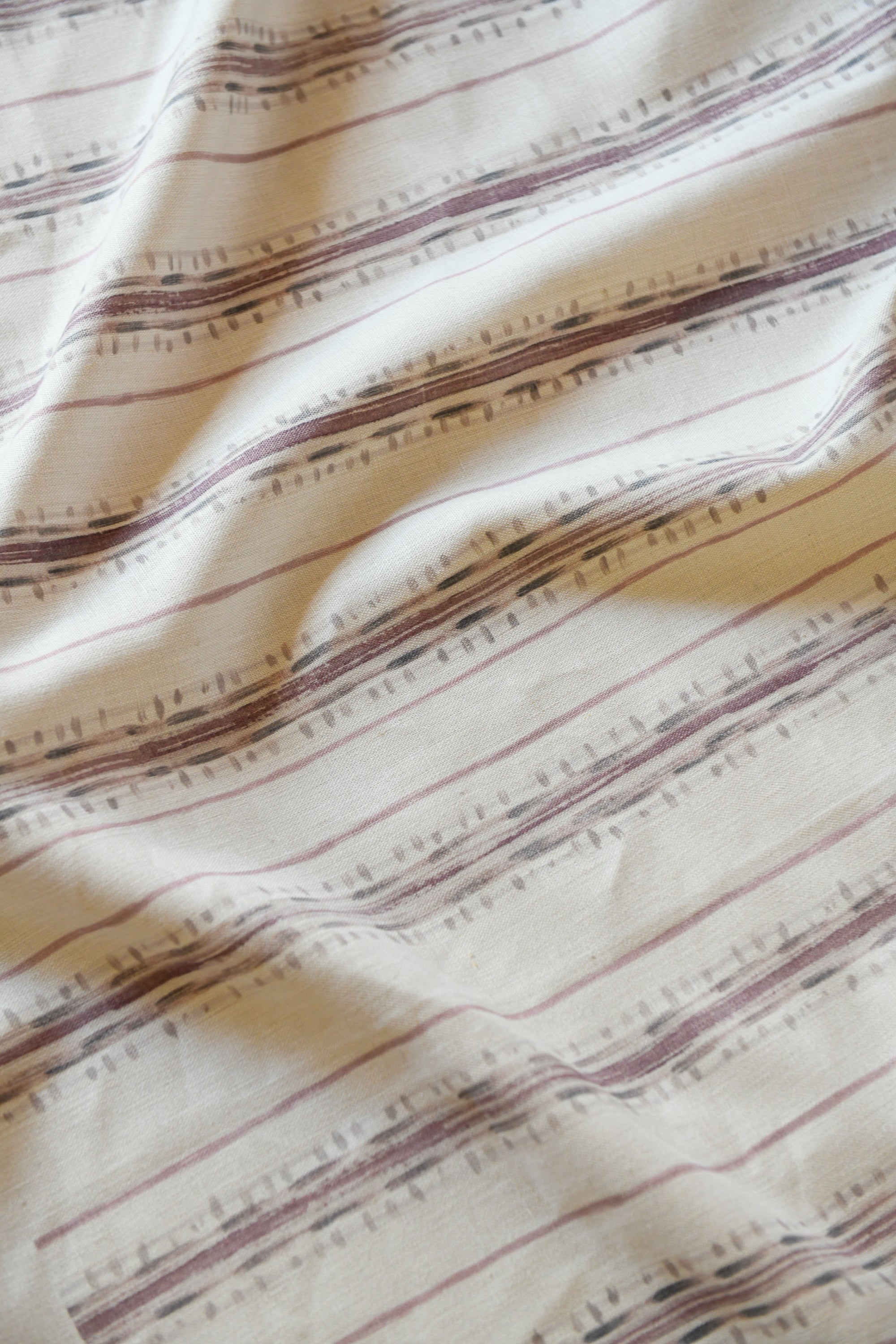 Close-up view of a pink striped pattern on a beige linen fabric.