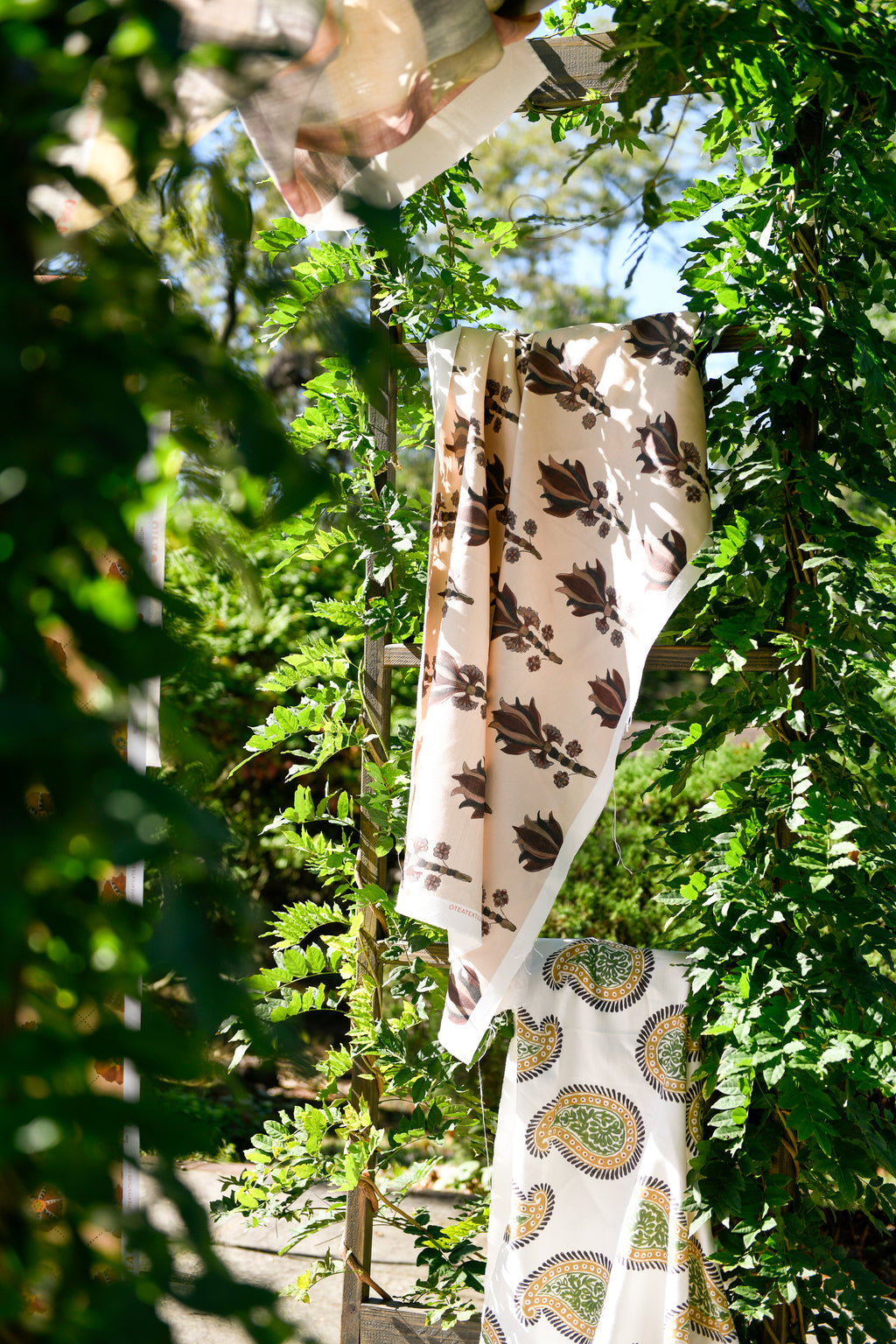 A yard of fabric with a floral pattern hanging outdoors among greenery.