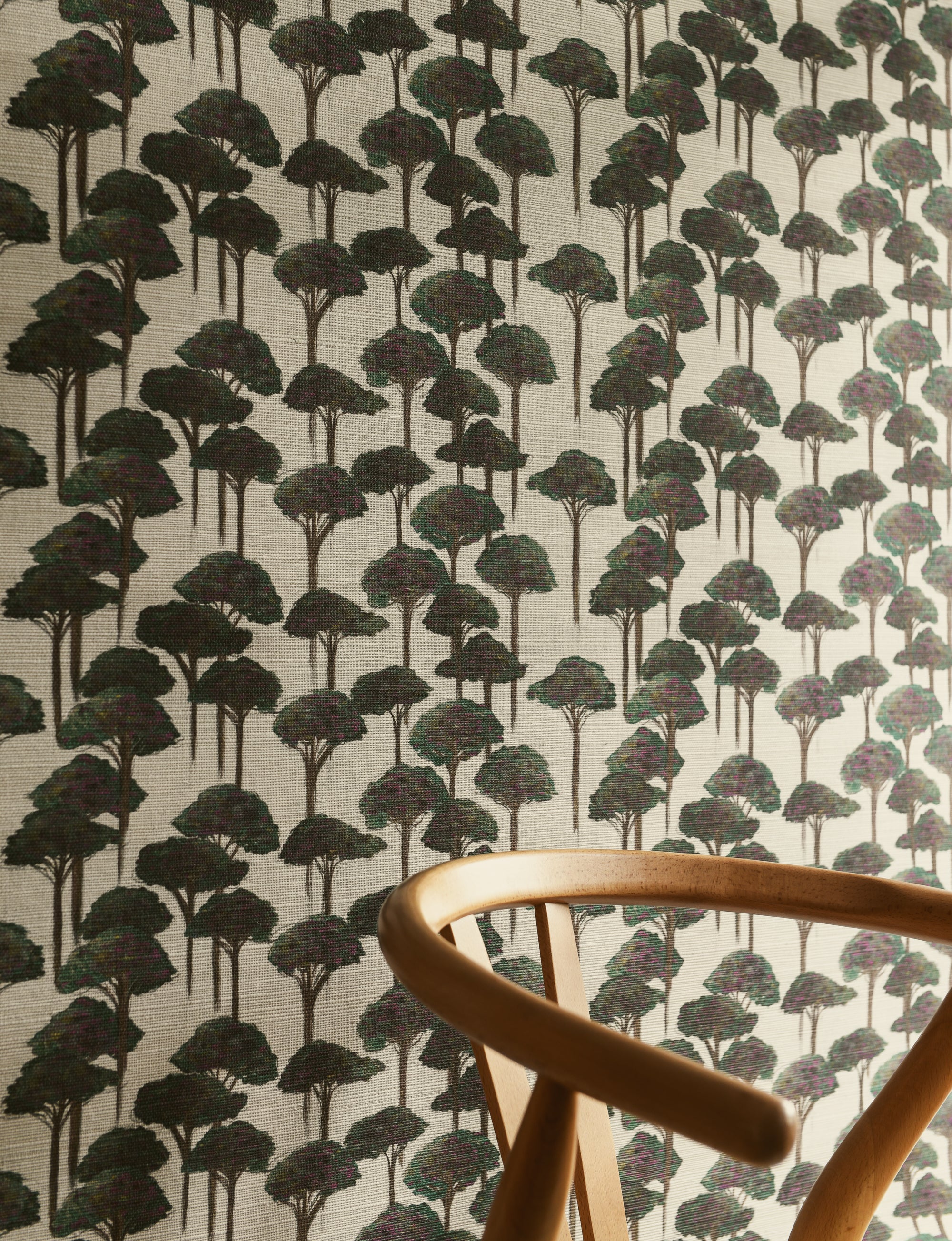 A section of wallpaper with a pattern of umbrella pines in various shades of gray and green on a light background, with part of a wooden chair visible in the frame.