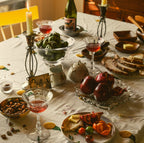 Dining table set with food, drinks, and decorative elements on a white tablecloth.