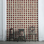 A room with Suzani wallpaper featuring a geometric pattern in red and white colors. Two chairs and a small table are placed against the wall, highlighting the wallpaper.