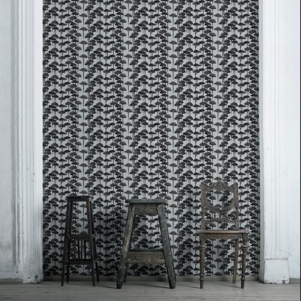 A room with Umbrella Pine Wallpaper featuring a geometric pine cone pattern in black and white. Two chairs are placed in front of the wallpapered wall.