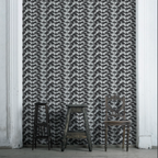 A room with Umbrella Pine Wallpaper featuring a geometric pine cone pattern in black and white. Two chairs are placed in front of the wallpapered wall.