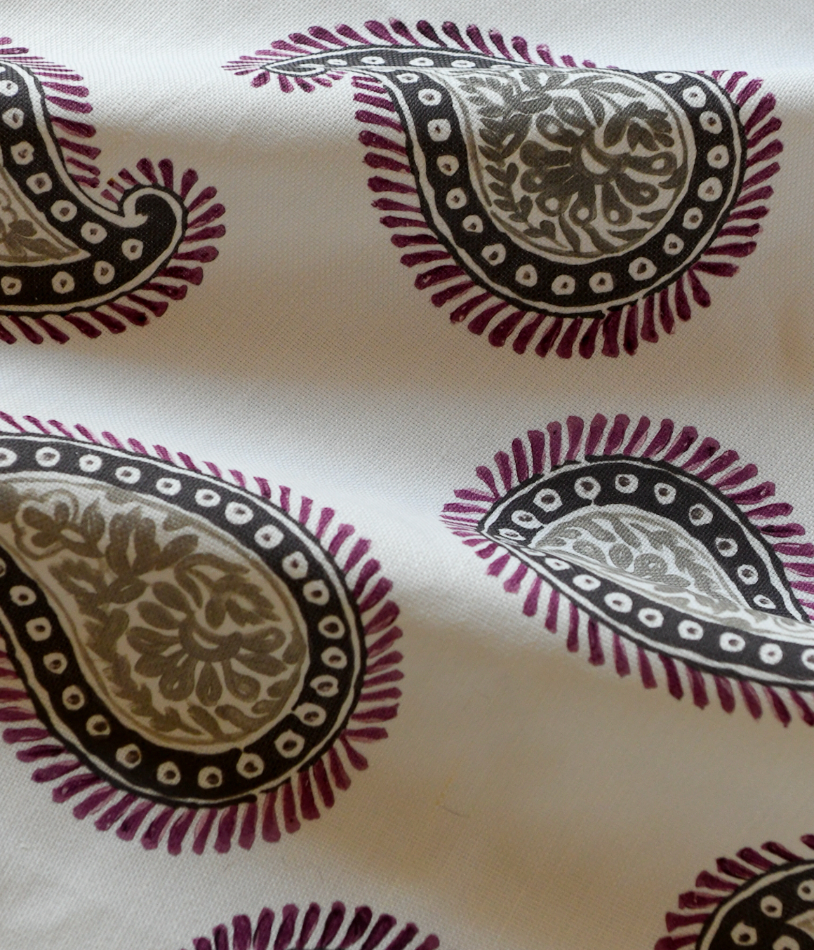 Close-up of a silk fabric with a paisley pattern featuring swirls and teardrop shapes, predominantly in beige and purple colors.