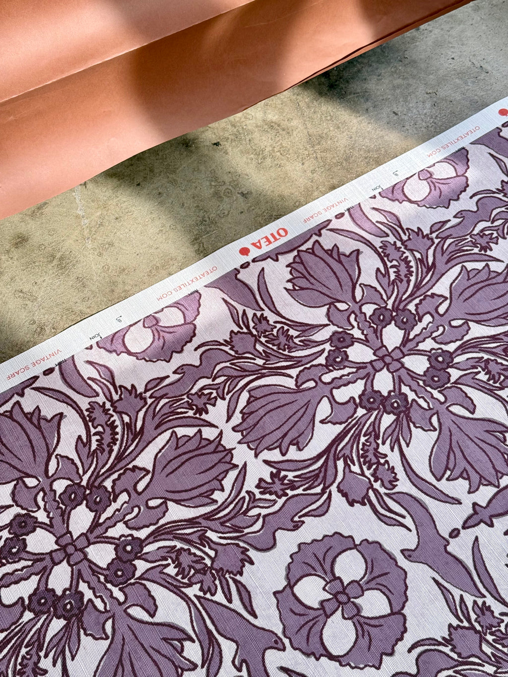 A close-up view of a wallpaper with a floral and geometric pattern in a purple hue on a light background.