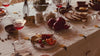 A dining table with glasses full of wine, pomegranates, orange peels, and bread and butter. there are old black and white photographs of people.