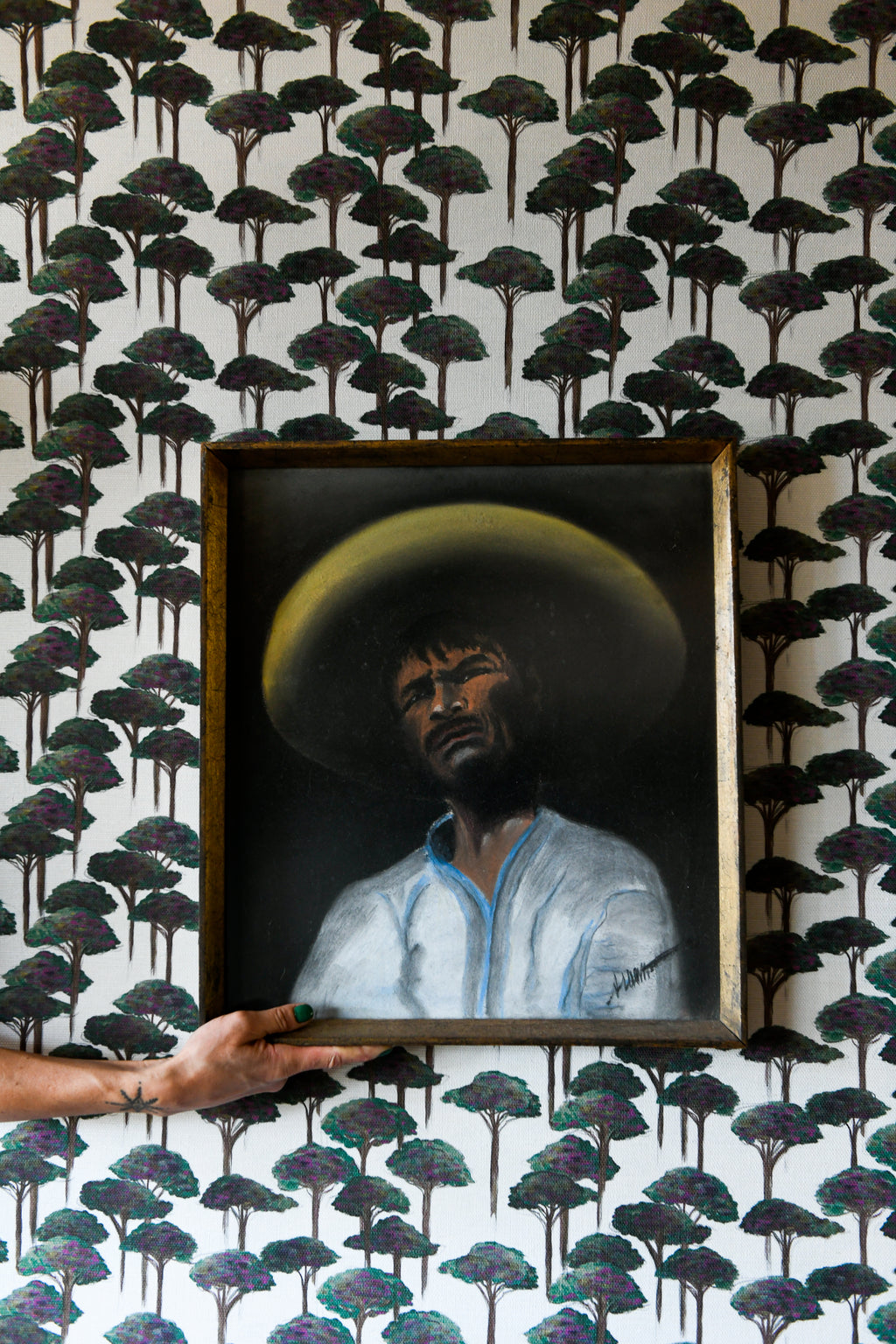 A section of wallpaper with a pattern of umbrella pines in various shades of gray and green on a light background, with part of a wooden chair visible in the frame.