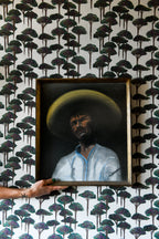 A section of wallpaper with a pattern of umbrella pines in various shades of gray and green on a light background, with part of a wooden chair visible in the frame.