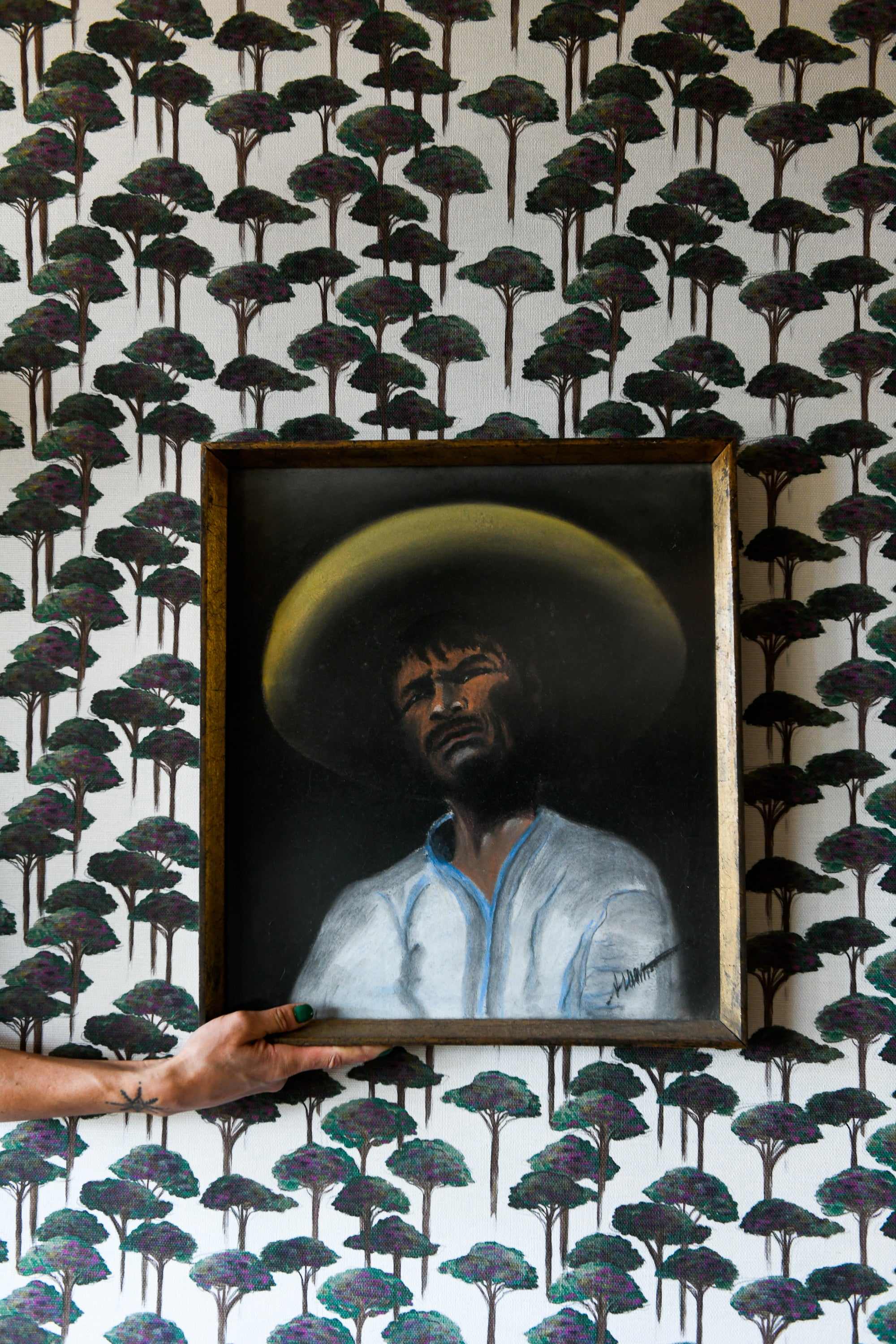 A section of wallpaper with a pattern of umbrella pines in various shades of gray and green on a light background, with part of a wooden chair visible in the frame.